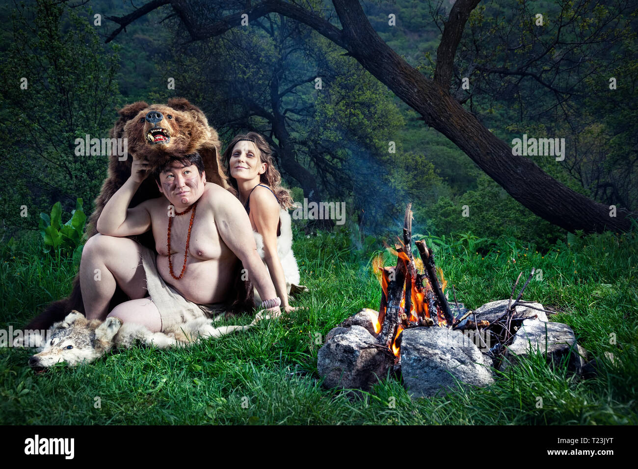 Grotta di persone vestite di pelle di animale seduto vicino a falò in foresta Foto Stock