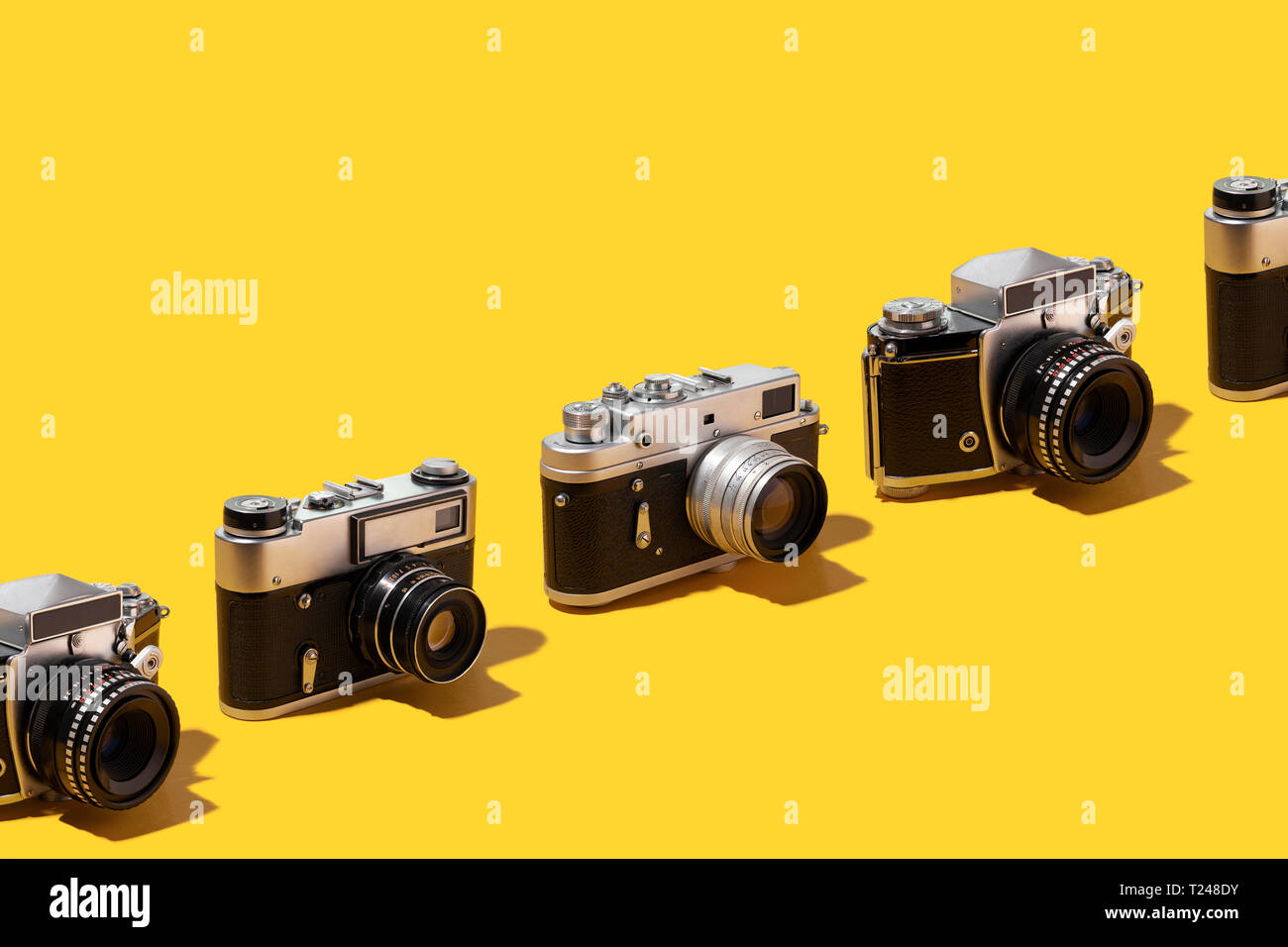 Le macchine fotografiche organizzate in una fila su sfondo giallo Foto Stock