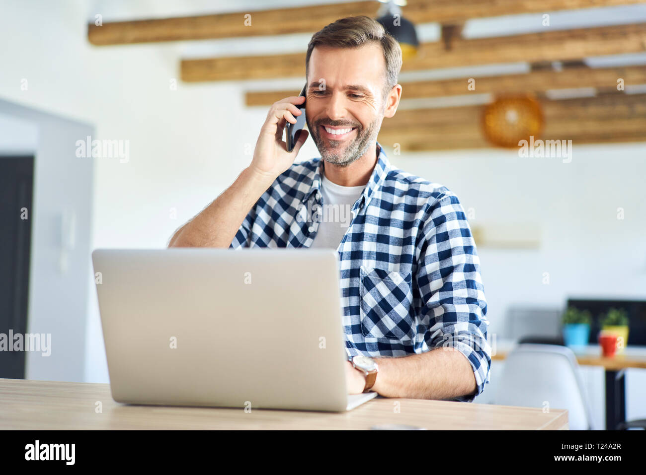 Uomo sorridente, parlando al telefono mentre si lavora da casa sul computer portatile Foto Stock