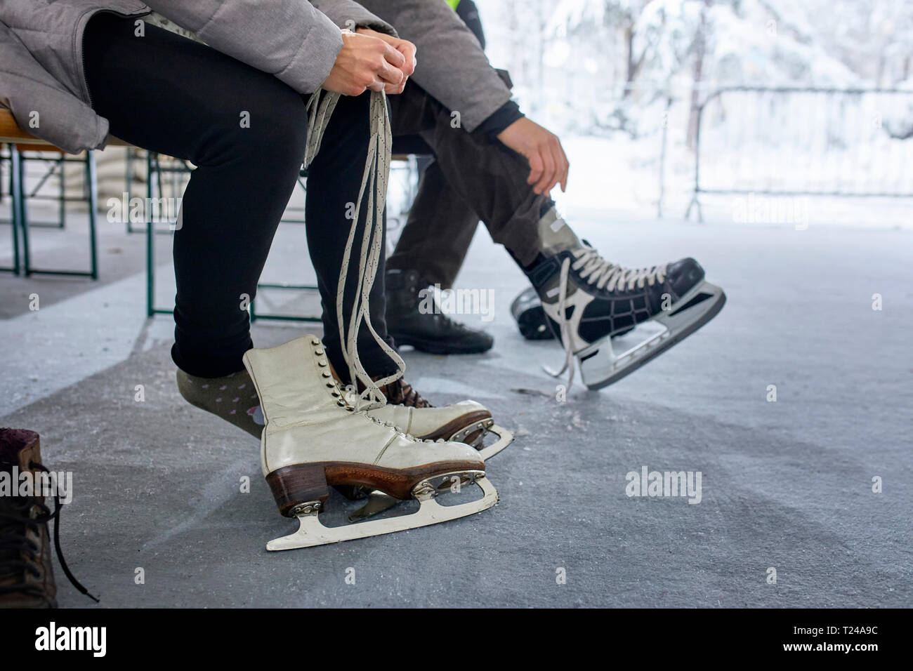Giovane seduto su un banco di lavoro presso la pista di pattinaggio su ghiaccio, mettendo su pattini da ghiaccio Foto Stock