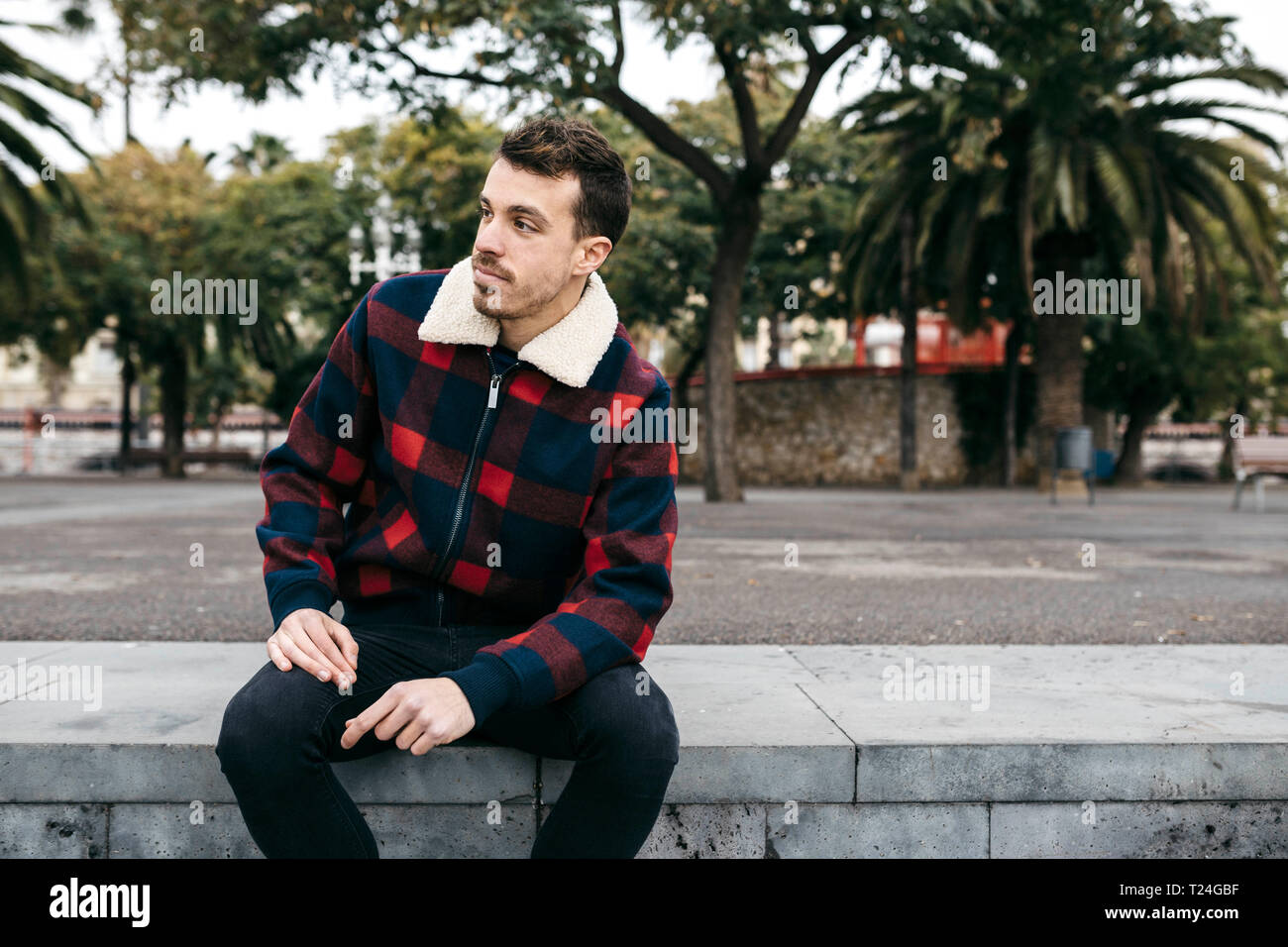 Giovane uomo che indossa abiti casual seduta su una panchina in città Foto Stock