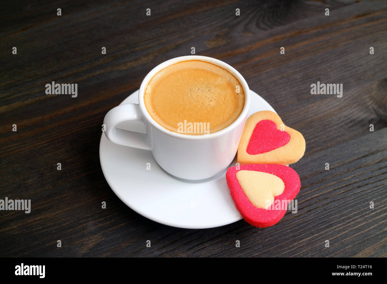 Una tazza di caffè caldo con una coppia di a forma di cuore i cookie sul colore scuro tavolo in legno Foto Stock