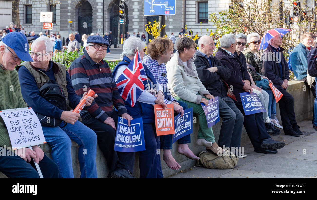 Westminster, Londra, Regno Unito; 29 marzo 2019; Fila di manifestanti Pro-Brexit sedersi su una parete durante il mese di marzo a lasciare Rally. Più tenere pro-Brexit segni Foto Stock