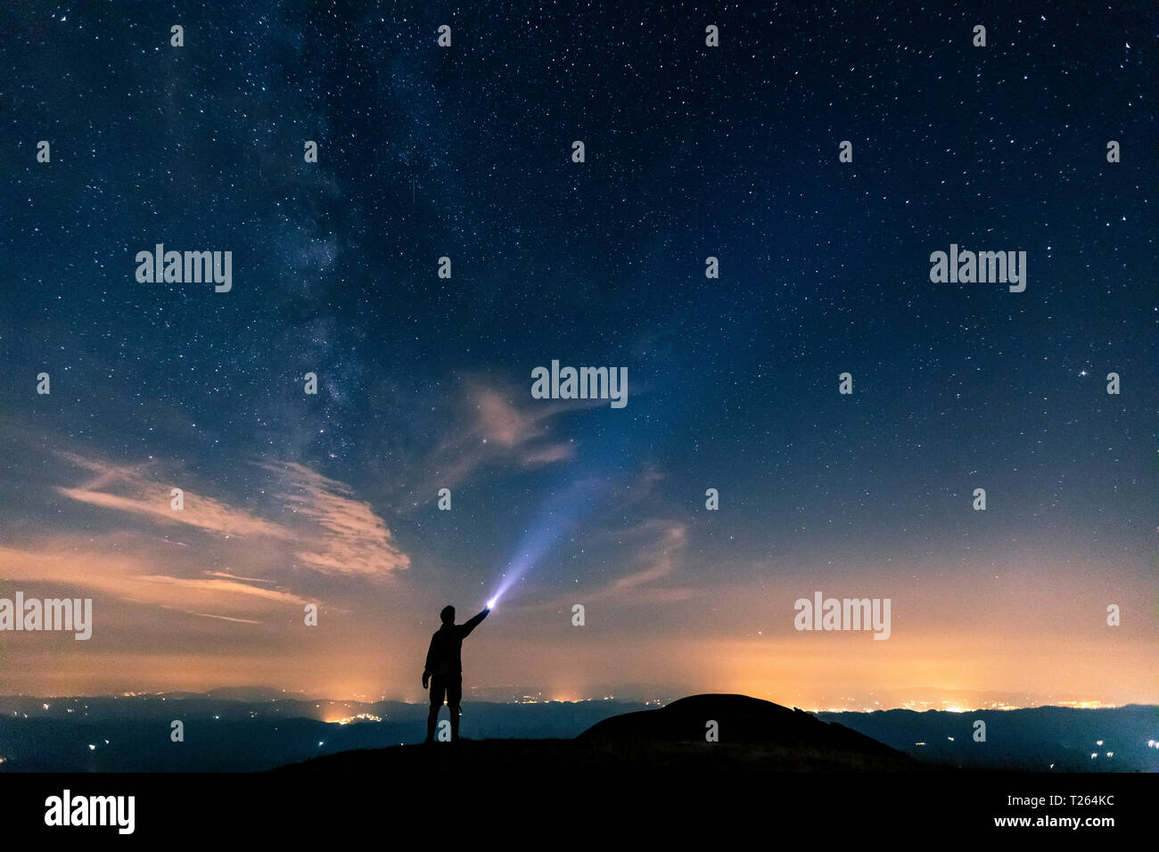 L'Italia, Monte Nerone, silhouette di un uomo con torcia sotto il cielo notturno con le stelle e la via lattea Foto Stock