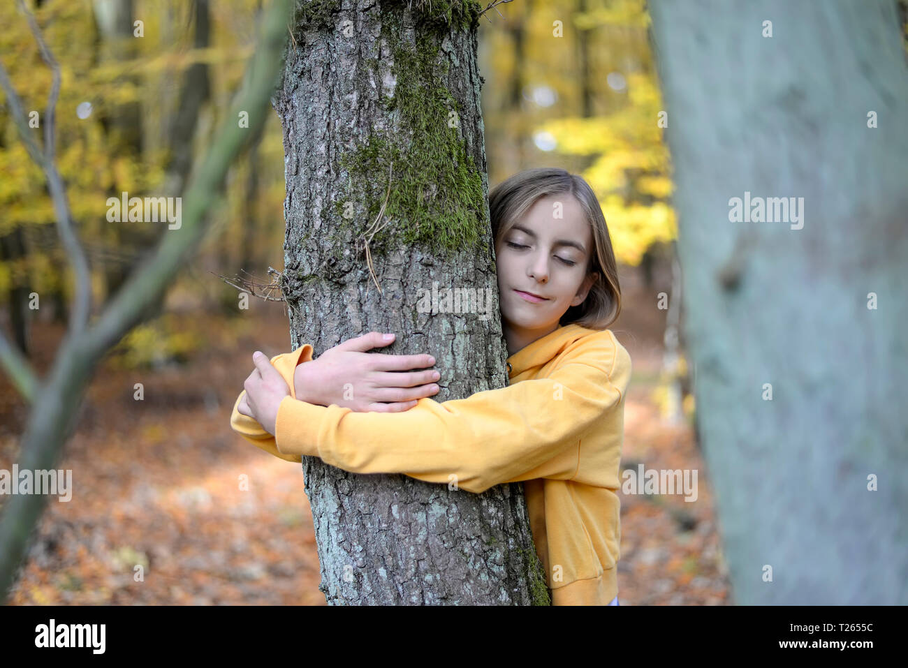 Ritratto di ragazza con gli occhi chiusi abbracciando albero nella foresta autunnale Foto Stock