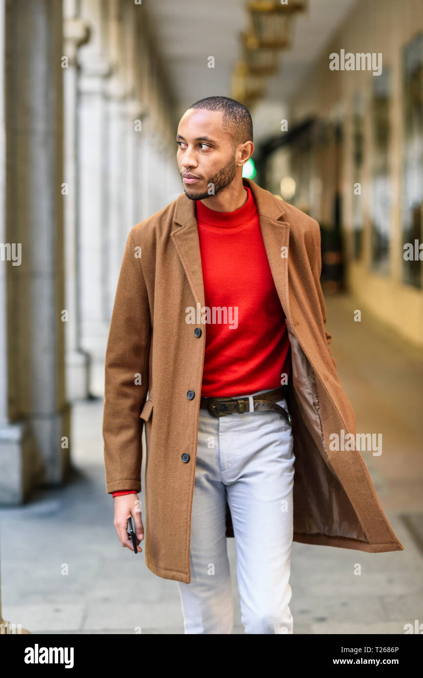 Moda giovane uomo che indossa maglione rosso e marrone cappotto camminando  lungo porticato Foto stock - Alamy