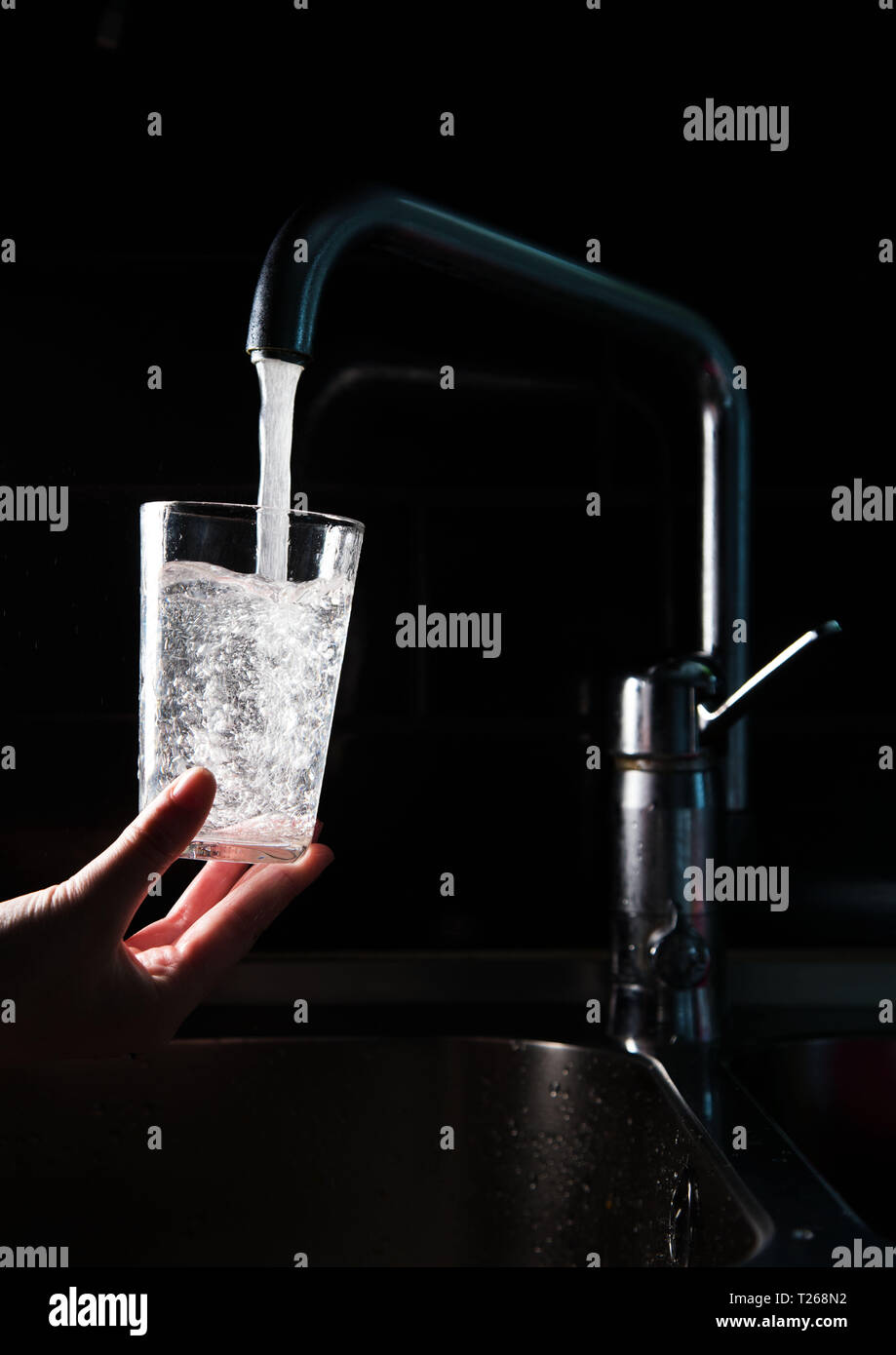 La carenza di acqua. Qualcuno si versa acqua in un bicchiere da un rubinetto in una cucina. Foto Stock