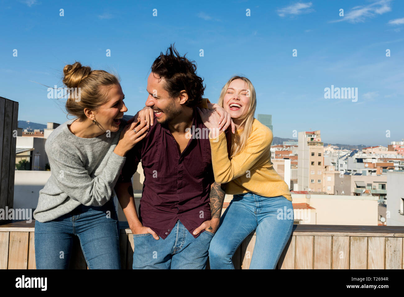 Amici seduti su un urbano terrazza sul tetto, con bracci intorno Foto Stock