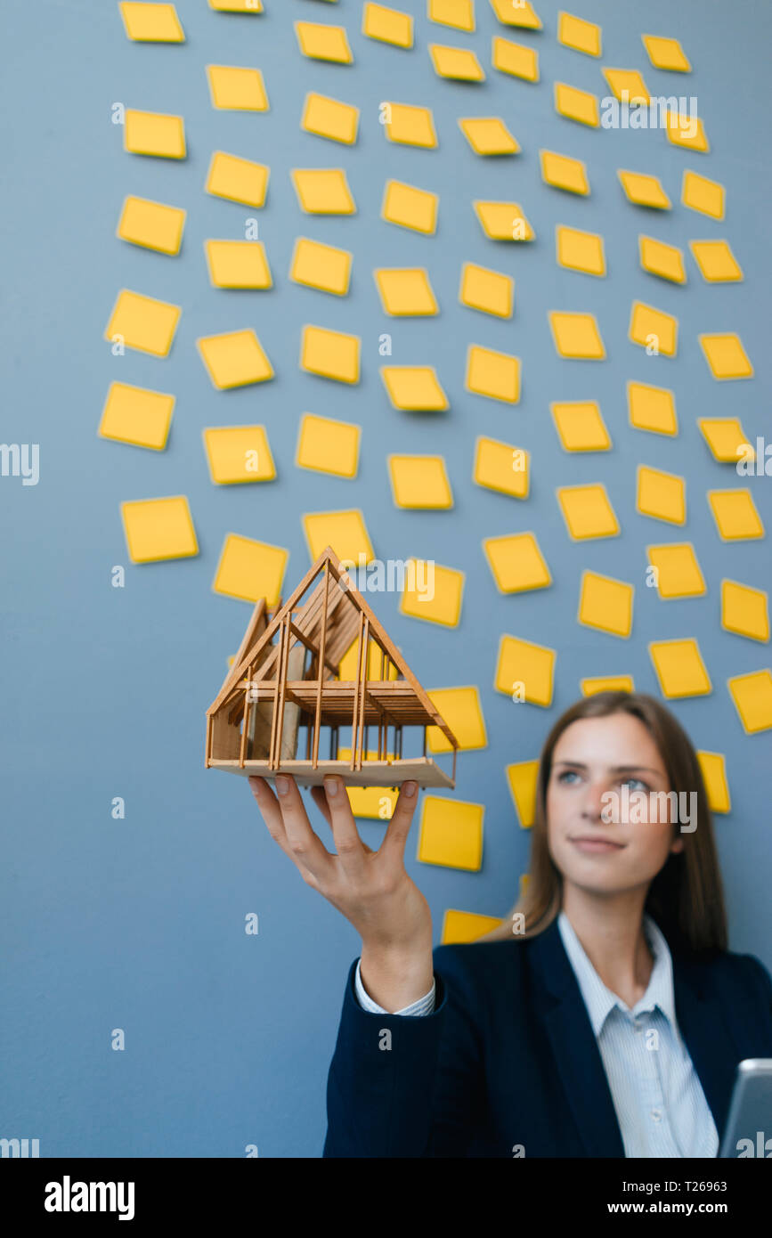 Giovane imprenditrice azienda modello architettonico con giallo sticky notes sulla parete dietro ger Foto Stock