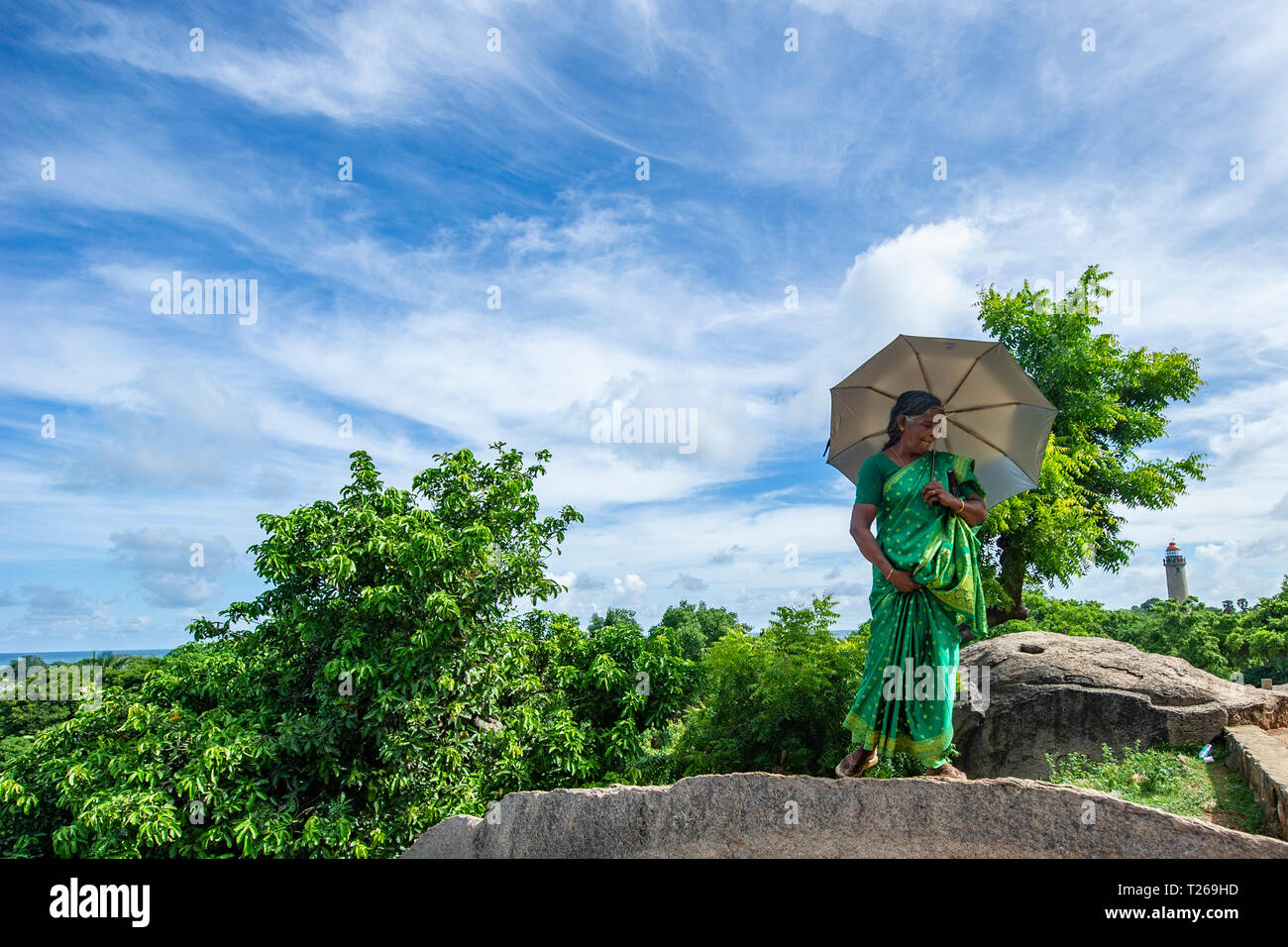 Eleganza presso i monumenti di Mahabalipuram vicino a Chennai, India come una donna passeggiate in campagna, proteggere se stessa dal sole con un ombrellone Foto Stock
