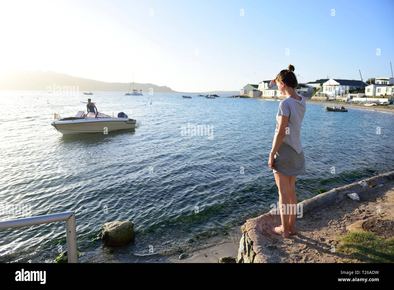 Giovane donna in piedi presso la costa alla ricerca di un uomo su una barca in mare Foto Stock