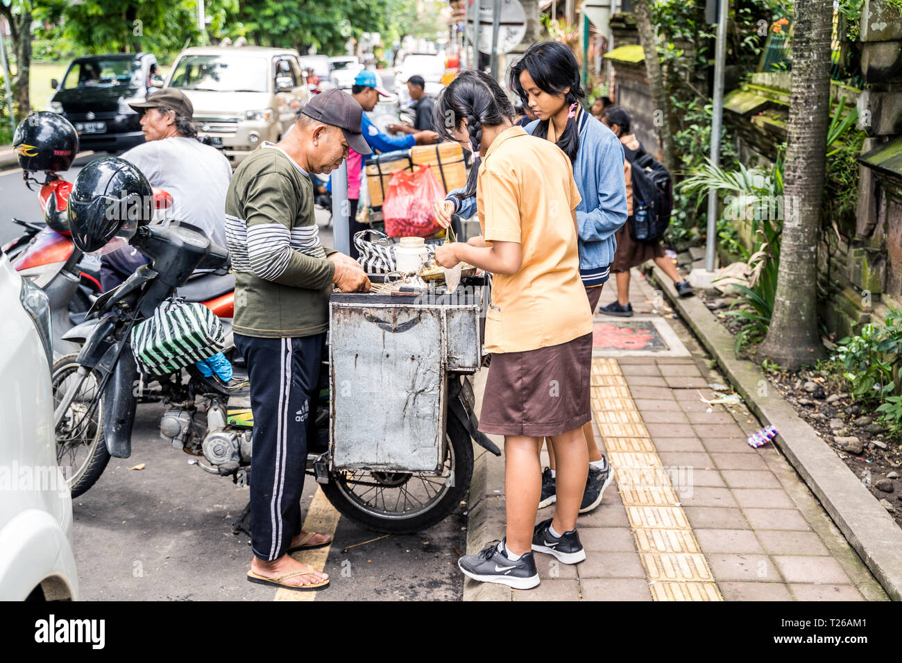 Ubud, Bali, Indonesia - Gennaio 2019: Ragazze in uniforme scolastica comprare generi alimentari da un venditore ambulante durante la pausa pranzo Foto Stock