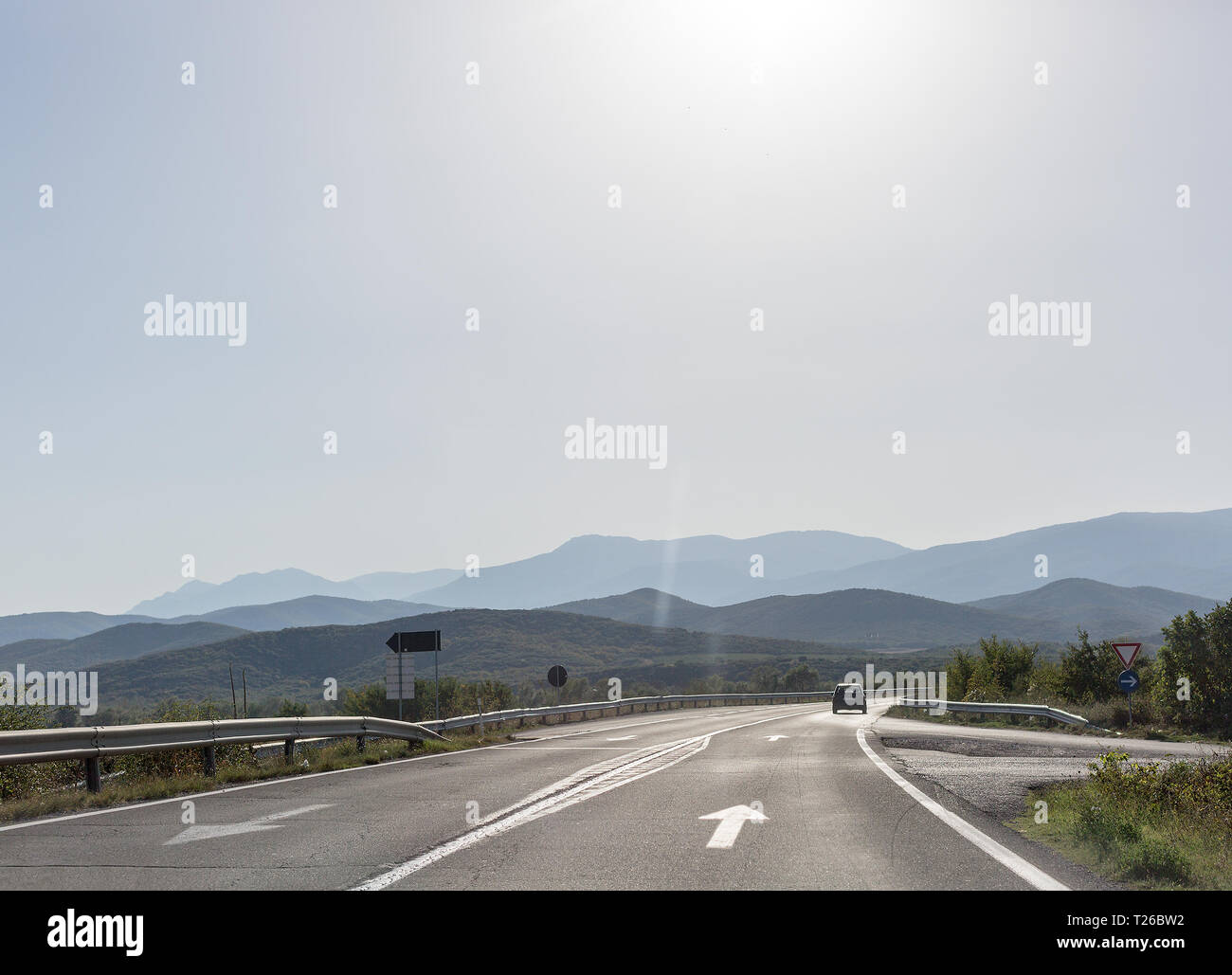 Strada asfaltata con un solitario auto sullo sfondo delle montagne. Spazio per il testo Foto Stock
