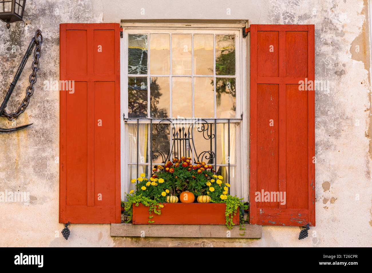Finestra esterna della storica casa coloniale con cassetta per fiori e persiane rosse Foto Stock