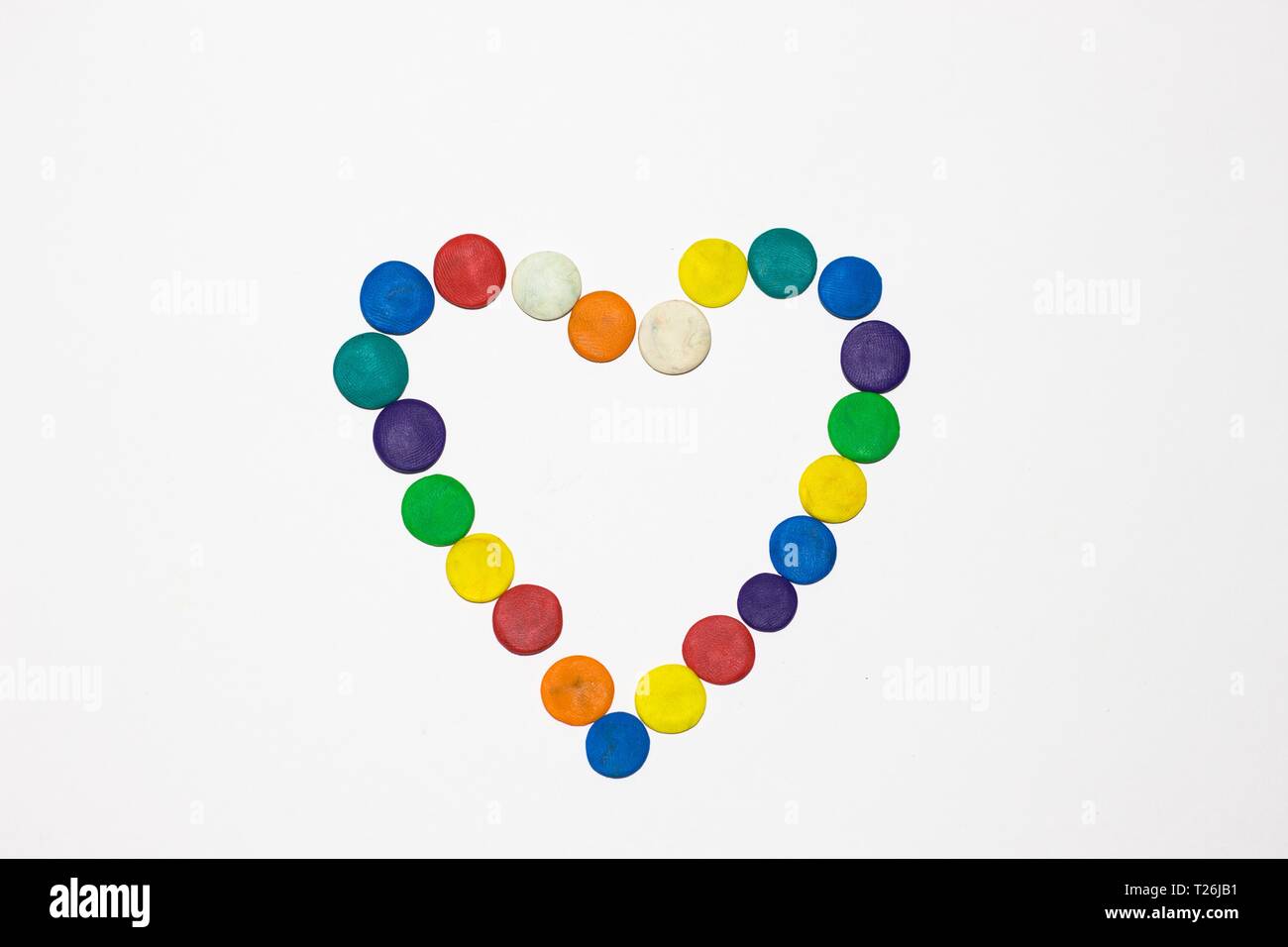 Il cuore di vari colori è riempito da cerchi che sono fatti di plastilina. Il cuore si trova su un libro bianco sullo sfondo. Foto Stock