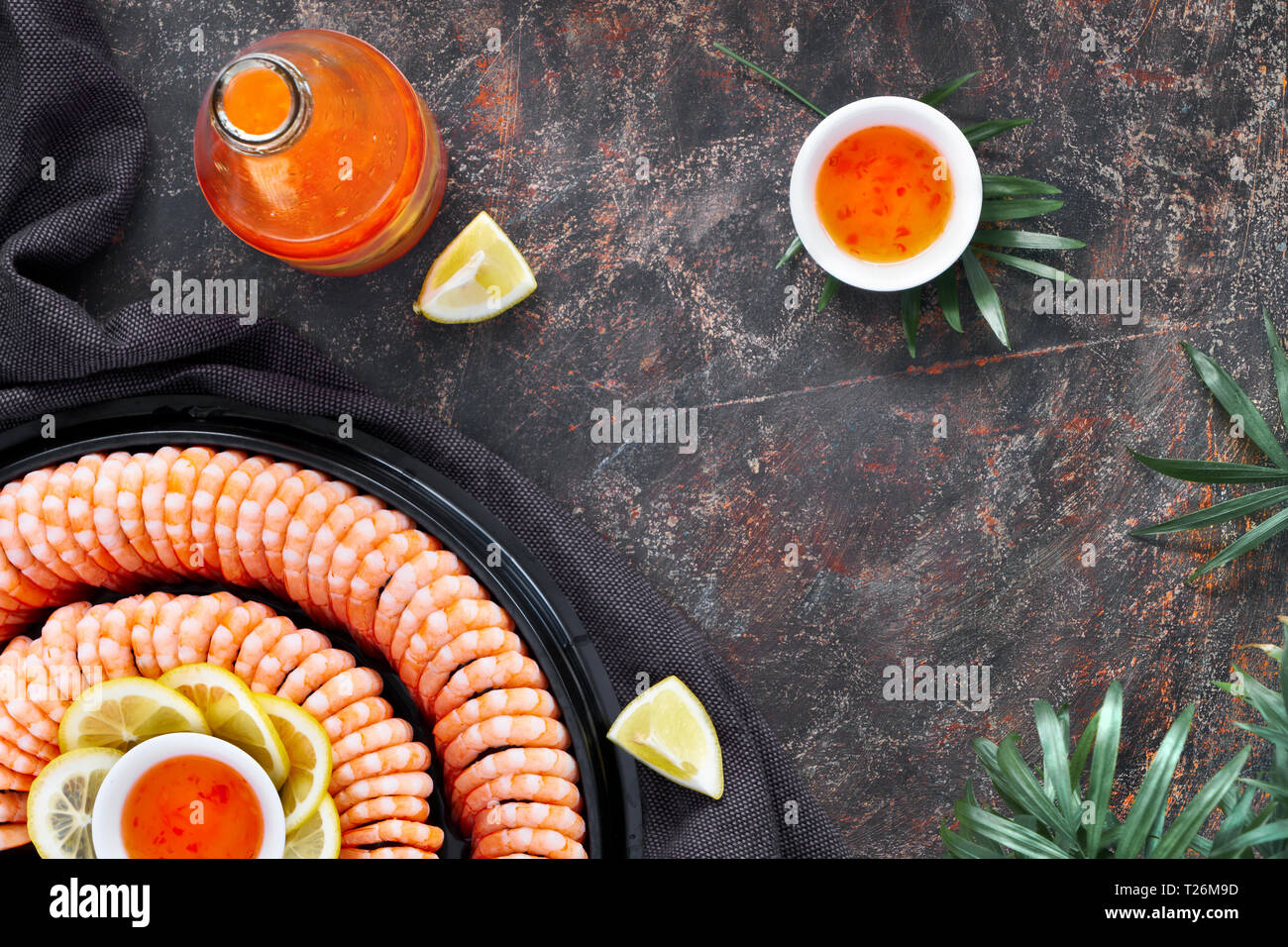 Il doppio anello di gustosi Gamberi serviti su una piastra scuro con limoni e salsa al peperoncino dolce, piatto laici scuro su sfondo a trama Foto Stock