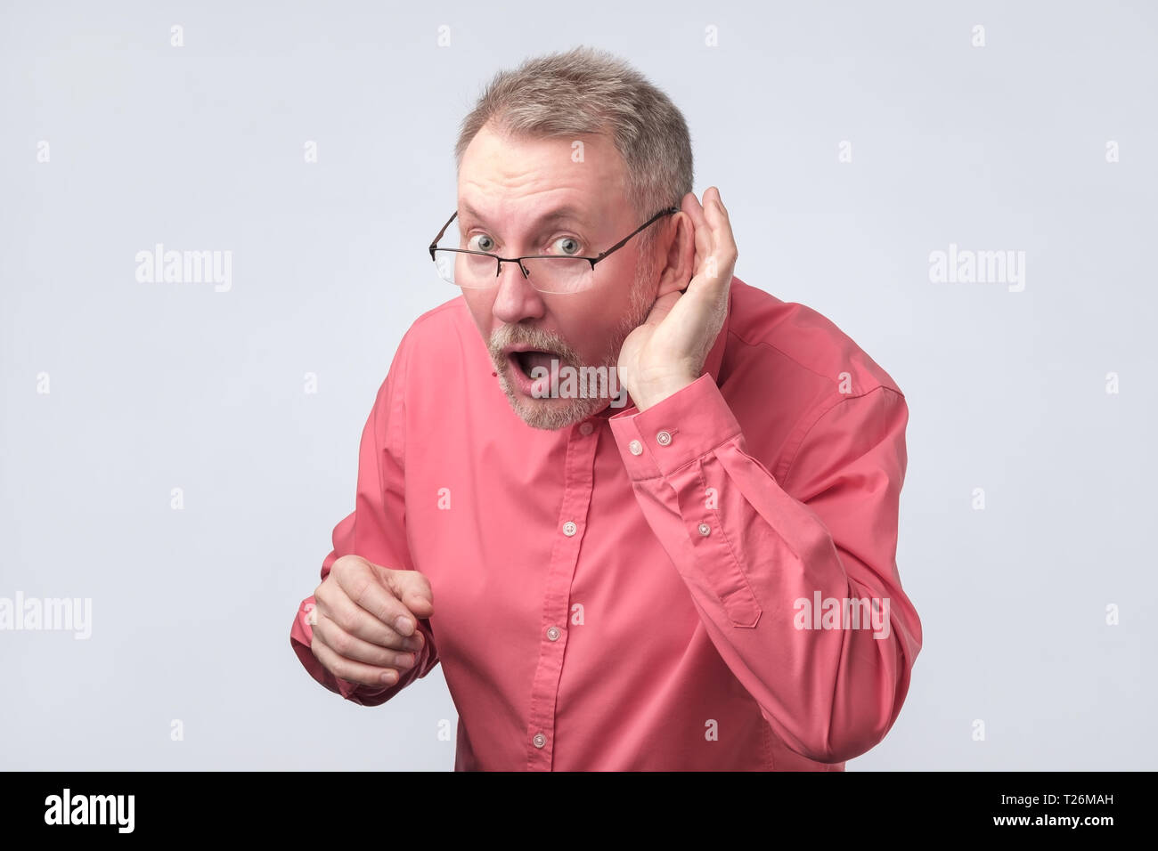 Senior Uomo in camicia rossa che soffre di sordità. Egli vuole sentire voci fresche. Foto Stock