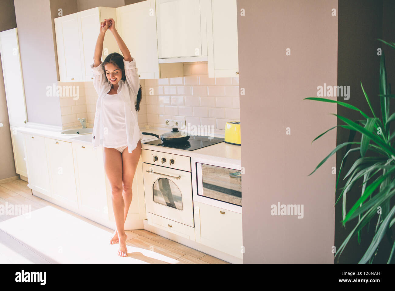 Buona e ben costruito bruna è lo stiramento fino e guardando verso il basso. Indossa una camicia bianca. La ragazza si trova in cucina Foto Stock