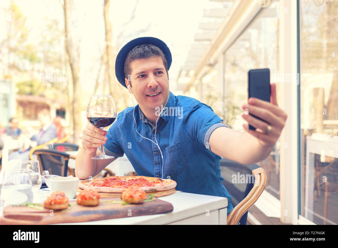 Hipster uomo prendendo selfie con grandi pizza e bruschetta mentre si tiene un bicchiere di vino rosso Foto Stock