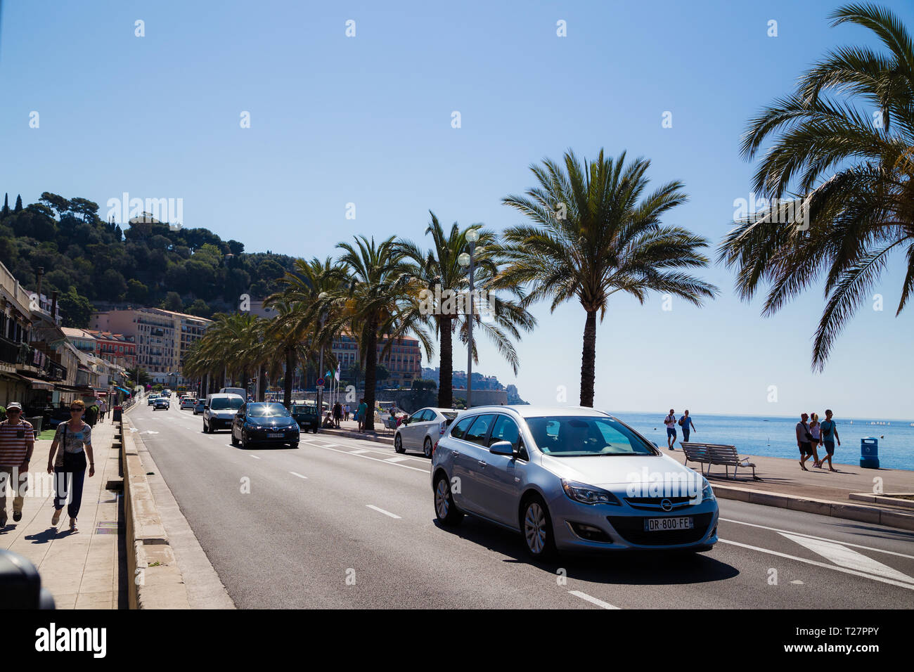 Promenade des Anglais, Nizza Francia. Palme lungo il lungomare offrono lo sfondo per le auto lungo la strada. Foto Stock