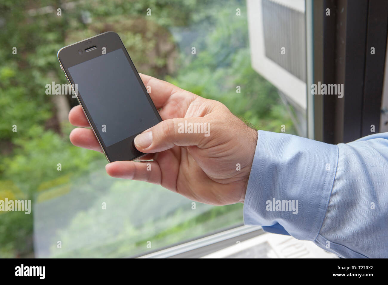 Mano d'uomo tenendo un martphone da una finestra Foto Stock
