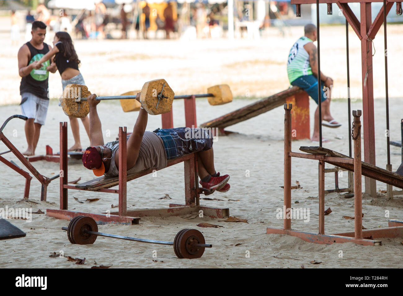 Un uomo lavora fuori facendo la pressa da banco con grezzo attrezzature di sollevamento pesi in una palestra a cielo aperto su di una spiaggia pubblica di Luglio 8, 2018 a Sao Vicente, Brasile. Foto Stock