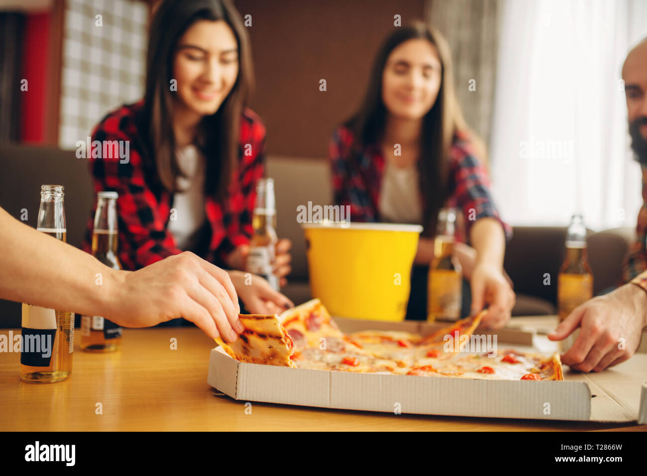 Sorridente amici bevande birra con la pizza a casa partito. Buona amicizia, gruppo di persone svaghi insieme. Allegra compagnia festeggiare l'evento Foto Stock
