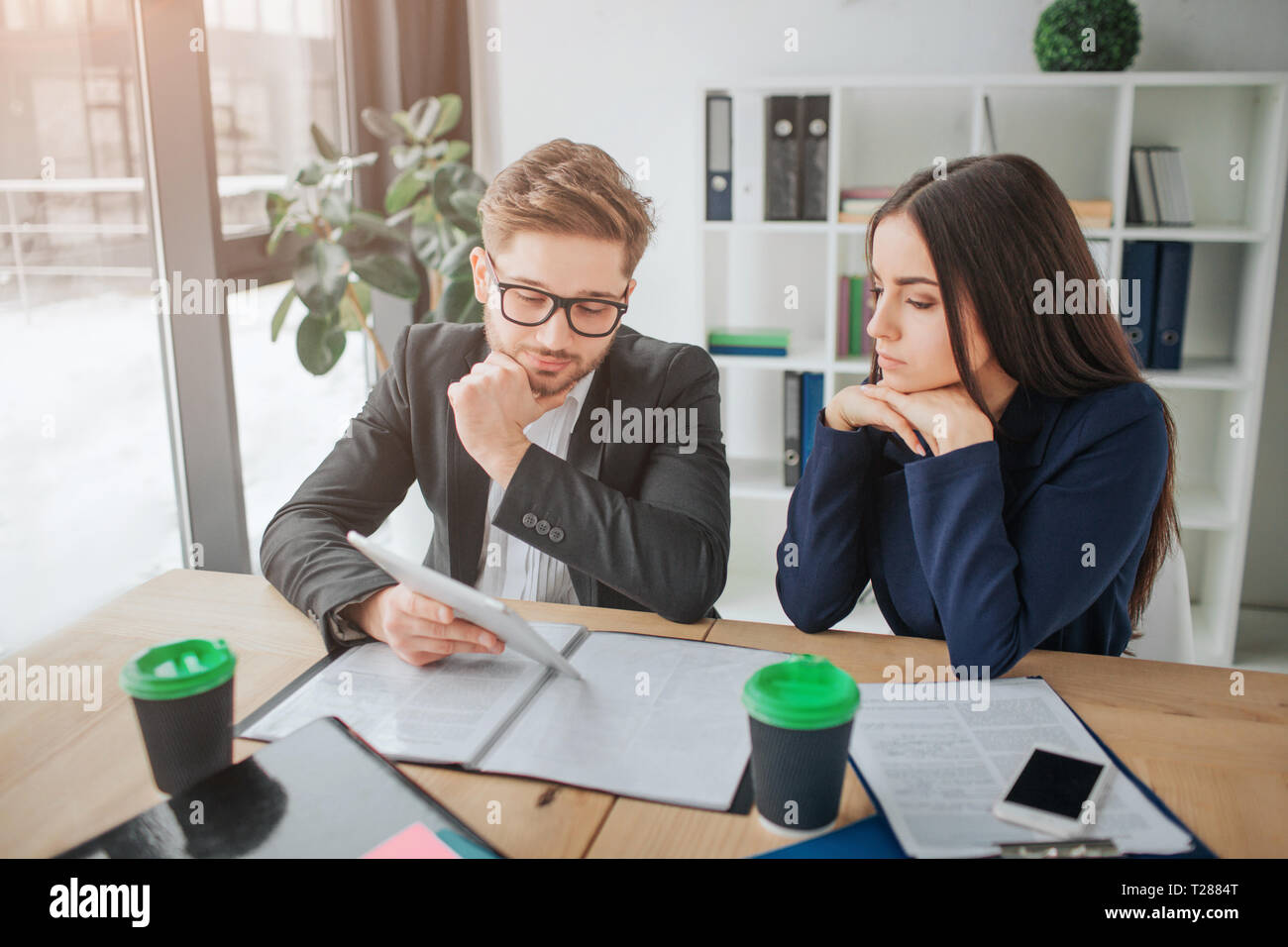 Occupato giovane uomo e donna si siedono a tavola in camera. Lo studio di un documento insieme. Le persone guardano pensierosi Foto Stock