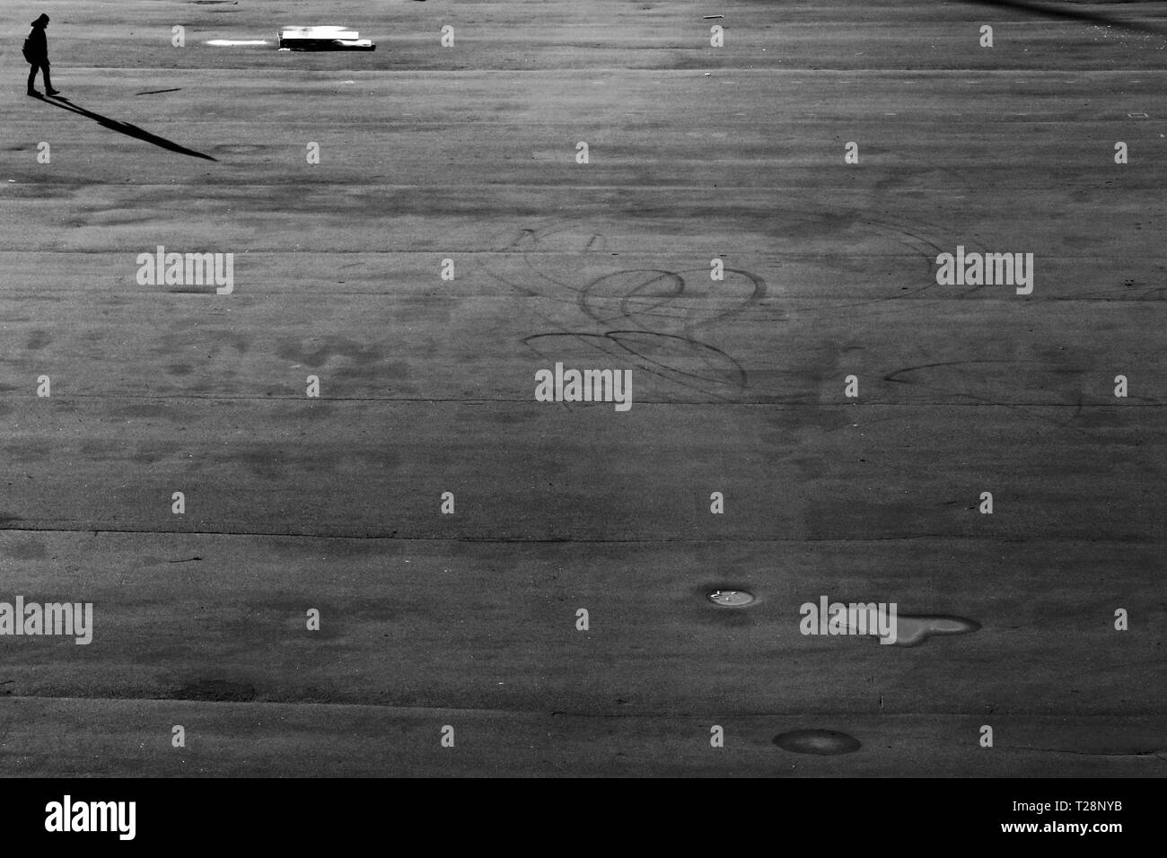 Un ragazzo cammina la distanza, in un grande pavimento esterno. Foto Stock