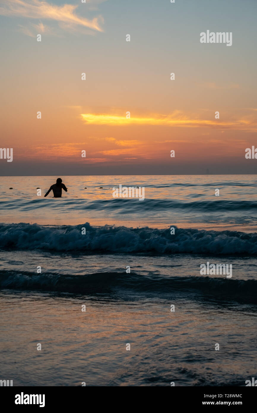 Un uomo tenendo bagno presso la spiaggia durante il tramonto Foto Stock