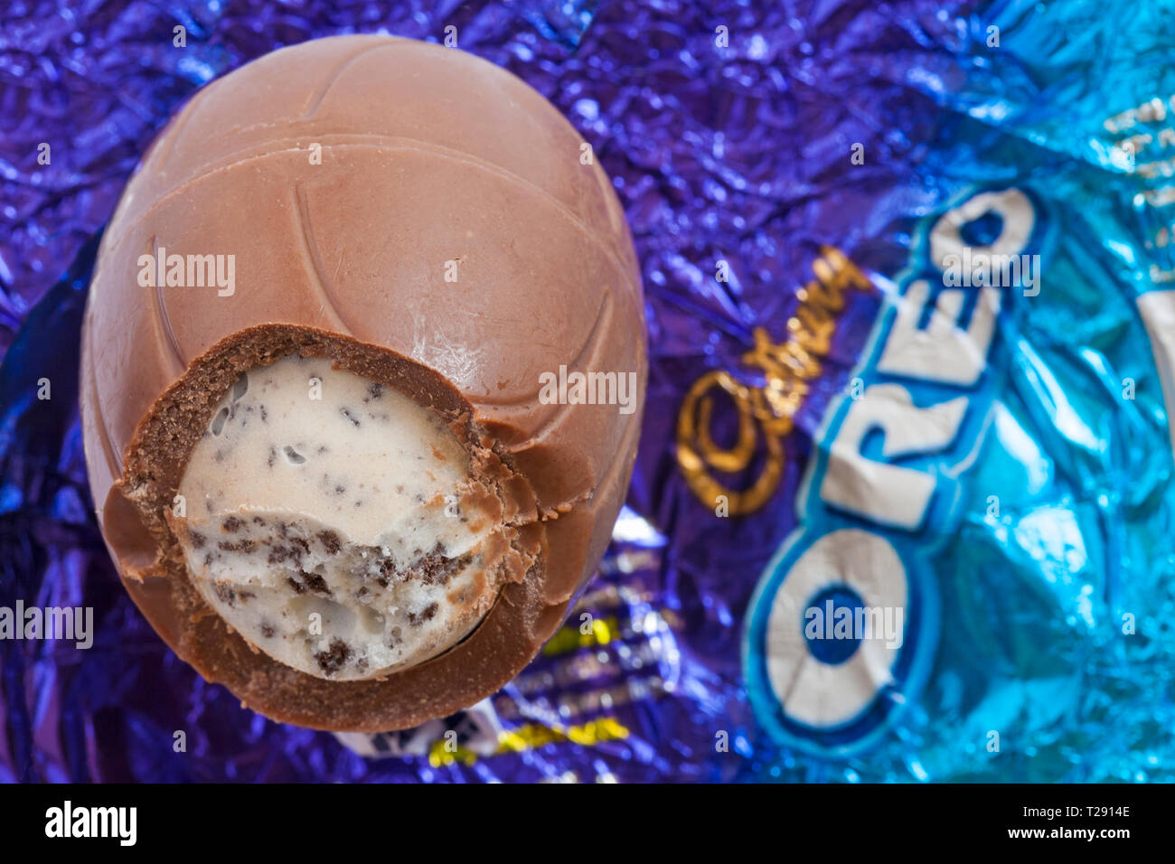 Oreo uovo di pasqua scartato e ha iniziato a mostrare il contenuto è stato impostato su involucro in foglio - latte uovo di cioccolato con una crema di latte ripieno e pezzi di biscotto Foto Stock