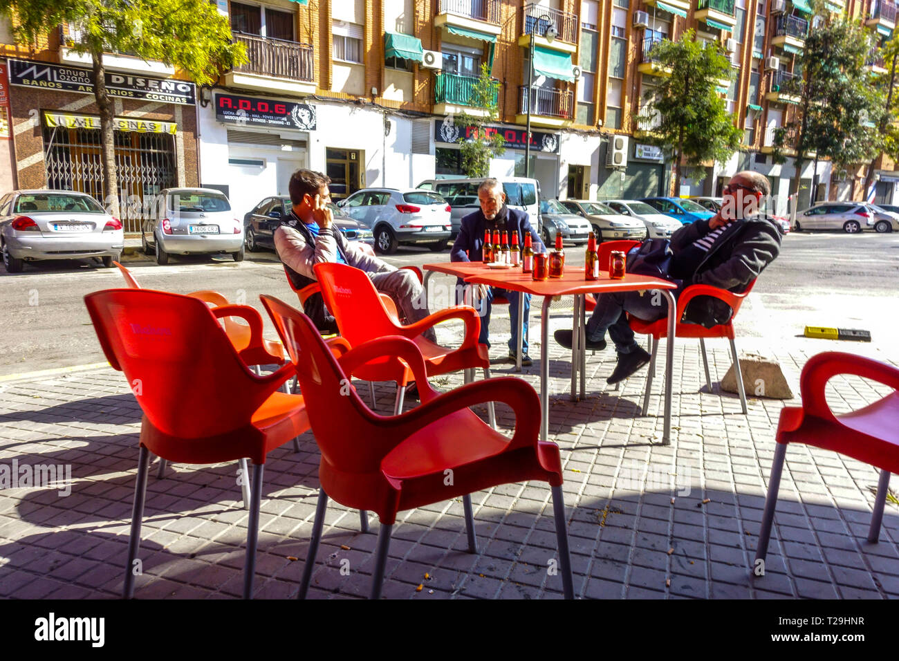 Tre uomini siedono fuori dal bar e bevono birra in bottiglia, il bar di Valencia Street Quart de Poblet, quartiere di Valencia, Spagna Foto Stock