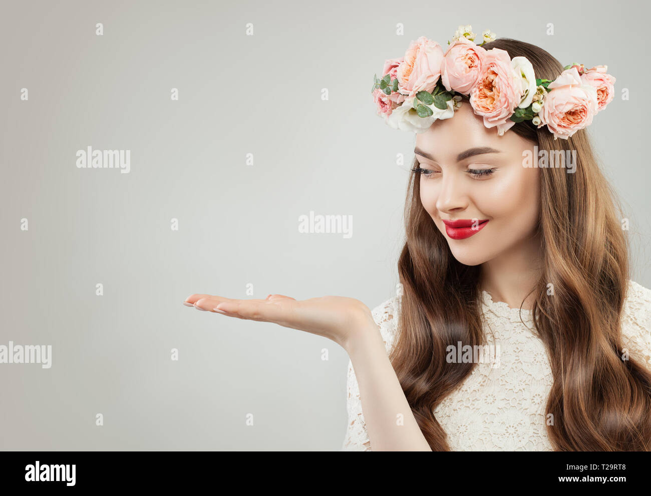 Piuttosto la molla modello donna guardando vuoto mano aperta con copia Spazio su uno sfondo bianco. Bellissima Ragazza con pelle chiara, capelli ricci, trucco e Flowe Foto Stock