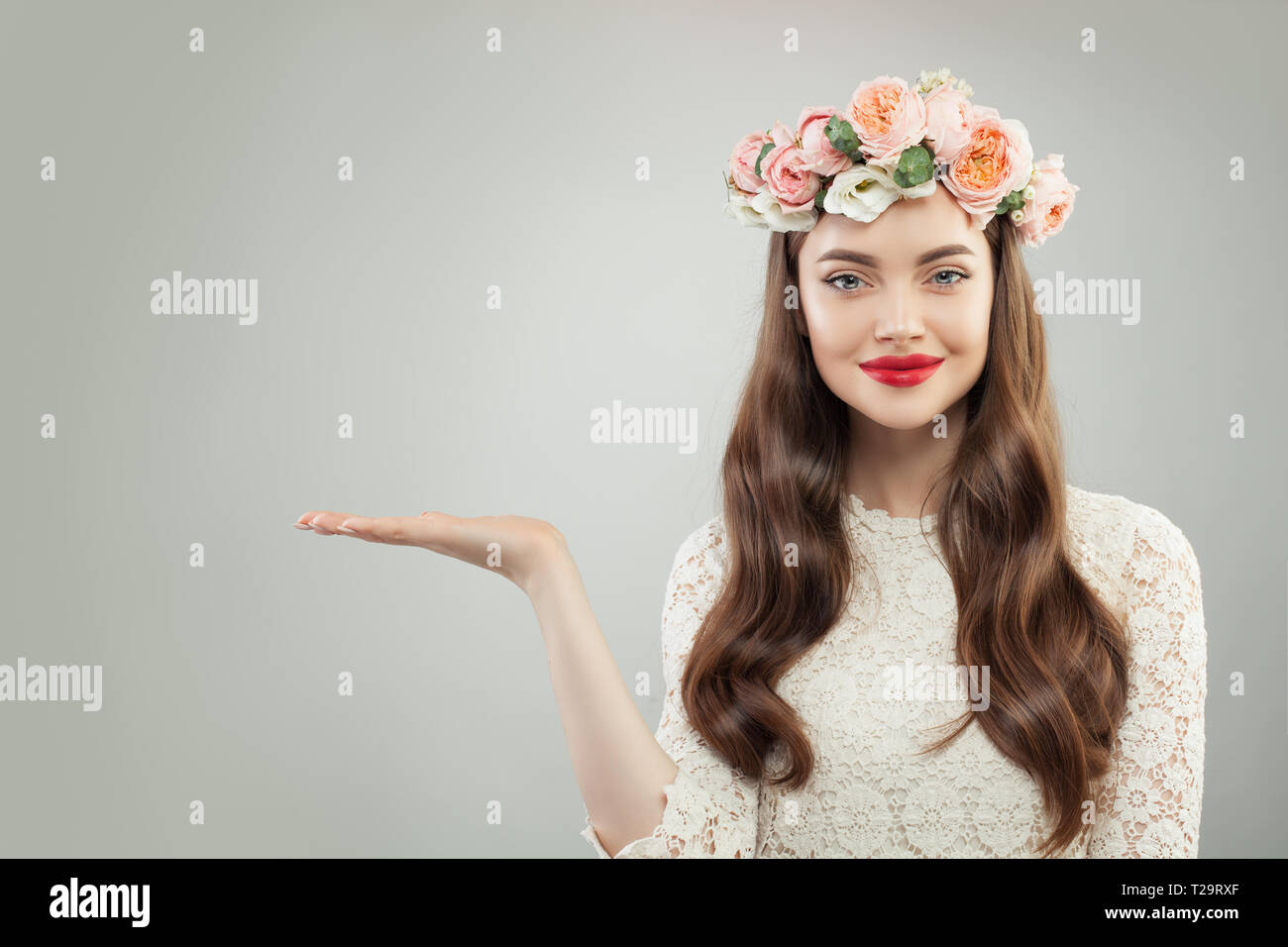 Bella Donna con vuoto aprire Palm mano con copia Spazio su uno sfondo bianco. Modello di graziosa ragazza con pelle chiara, capelli ricci, trucco e fiori. Adve Foto Stock