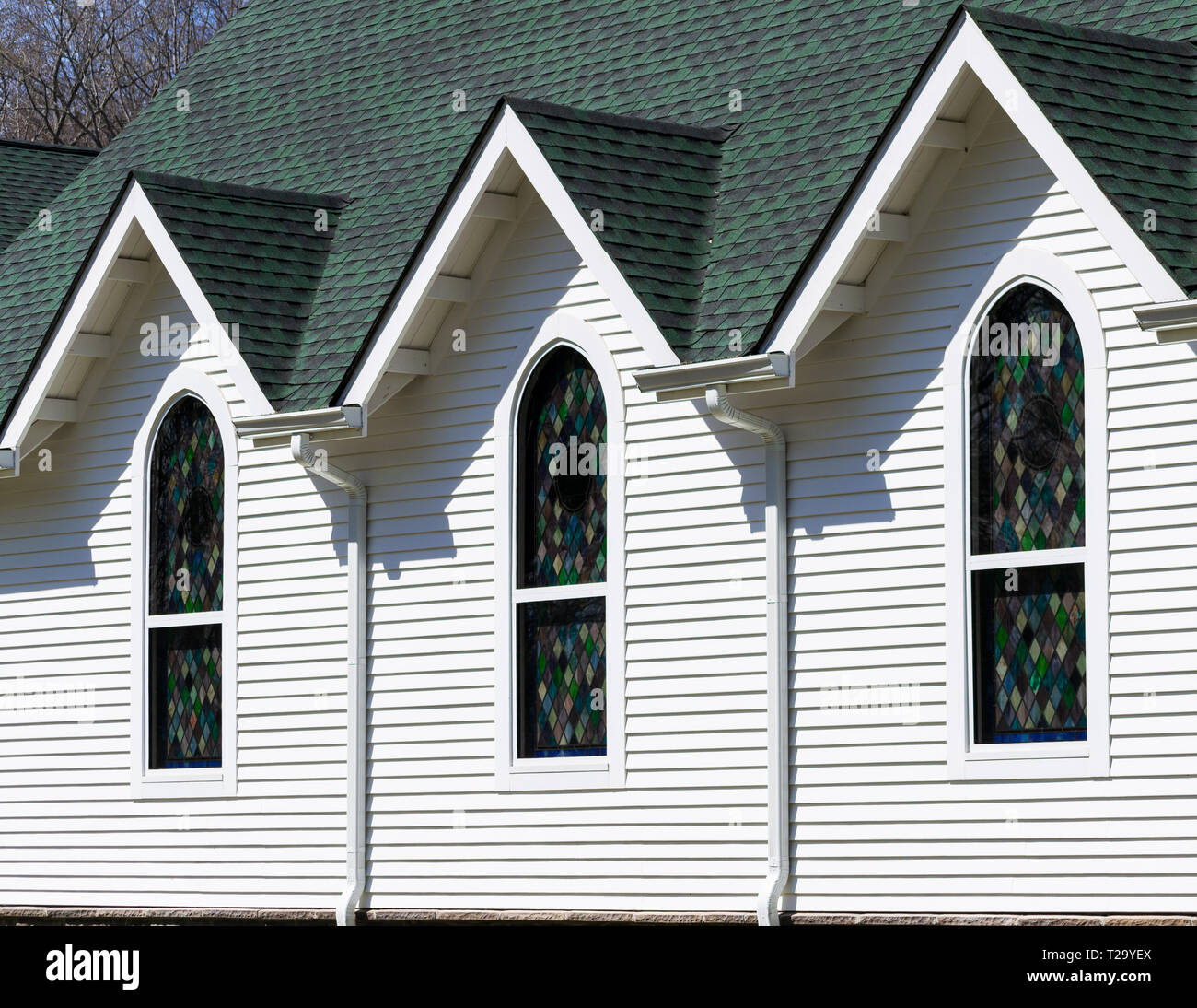 Obliqua di vista esterna di color verde scuro e tetto bianco luminoso con parete della chiesa, con tre tetto triangolare gables al di sopra di tre finestre di vetro colorato Foto Stock