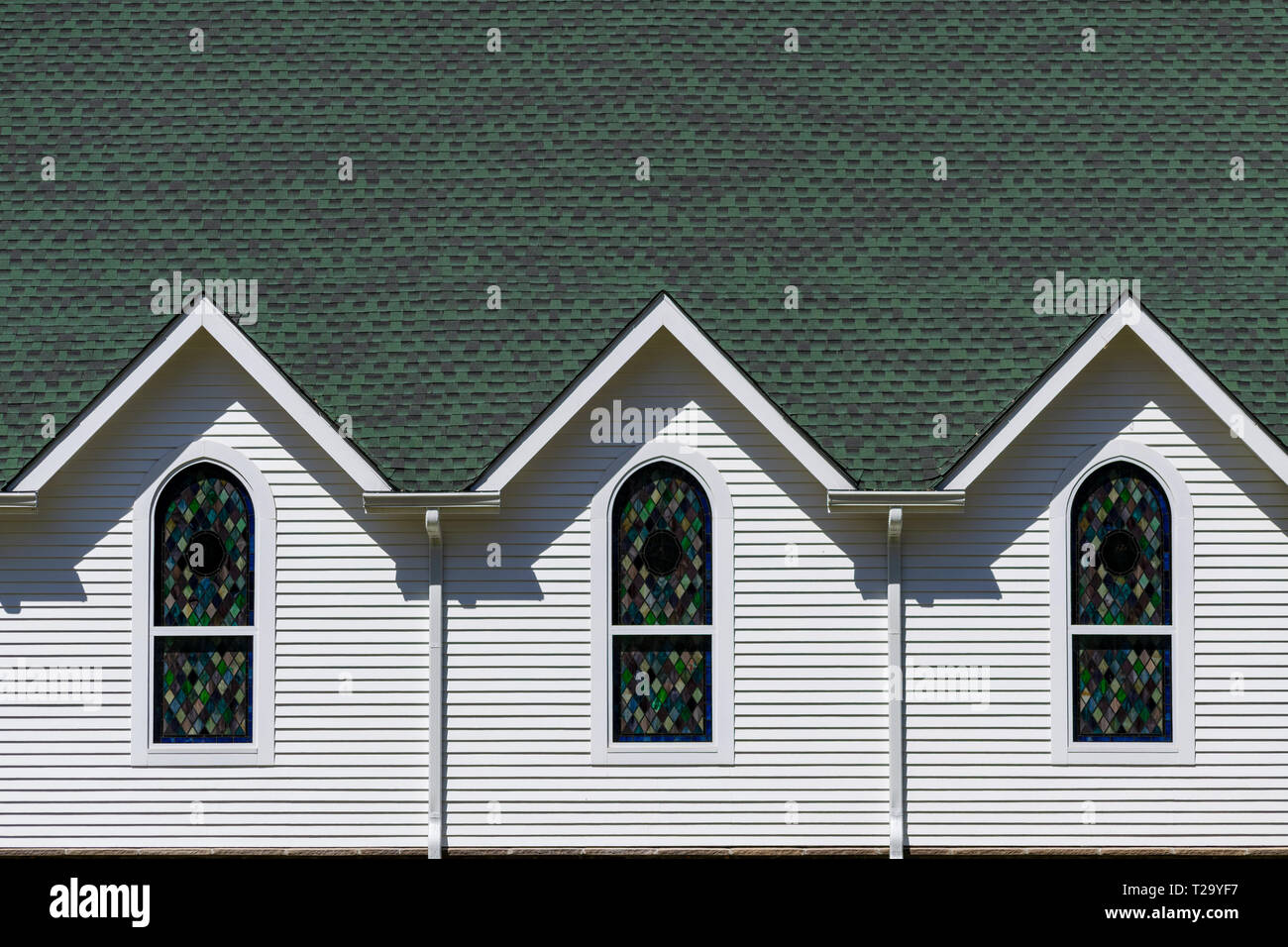 Vista esterna di color verde scuro e tetto bianco luminoso con parete della chiesa, con tre tetto triangolare gables al di sopra di tre finestre di vetro colorato Foto Stock