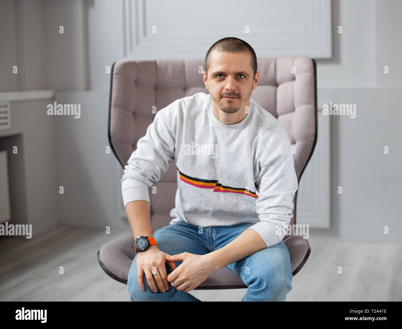 Ritratto di uomo che guarda in telecamera mentre seduti su una sedia nella moderna sala luminosa Foto Stock