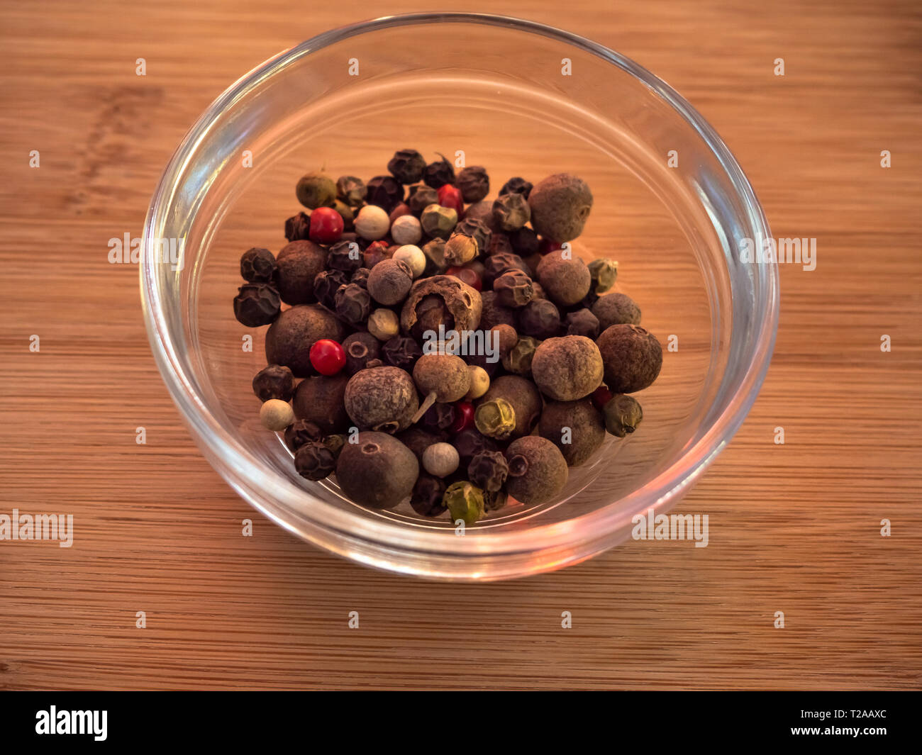Ciotola di cristallo con pepe bianco con cinque peperoni mix su una tavola di legno Foto Stock
