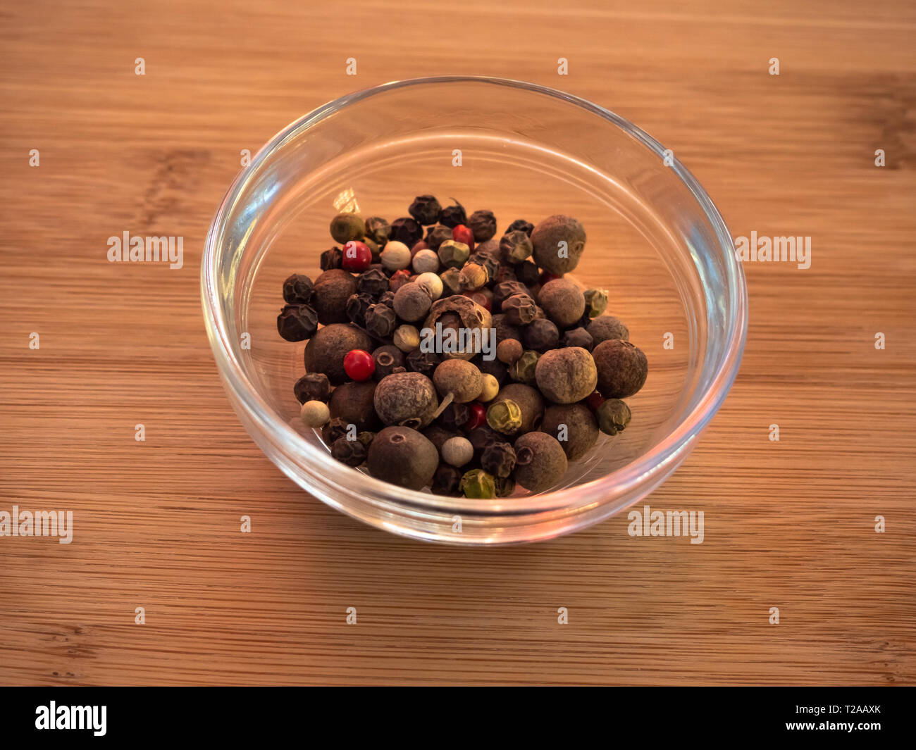 Ciotola di cristallo con pepe bianco con cinque peperoni mix su una tavola di legno Foto Stock