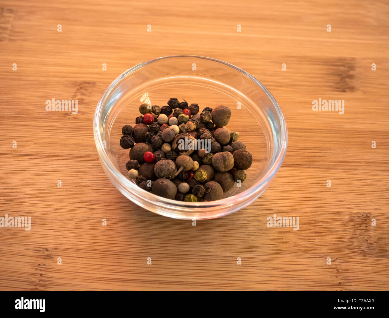 Ciotola di cristallo con pepe bianco con cinque peperoni mix su una tavola di legno Foto Stock