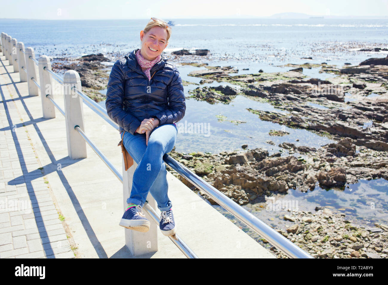 Donna seduta sulla ringhiera lungo Sea Point Promenade, Città del Capo Foto Stock