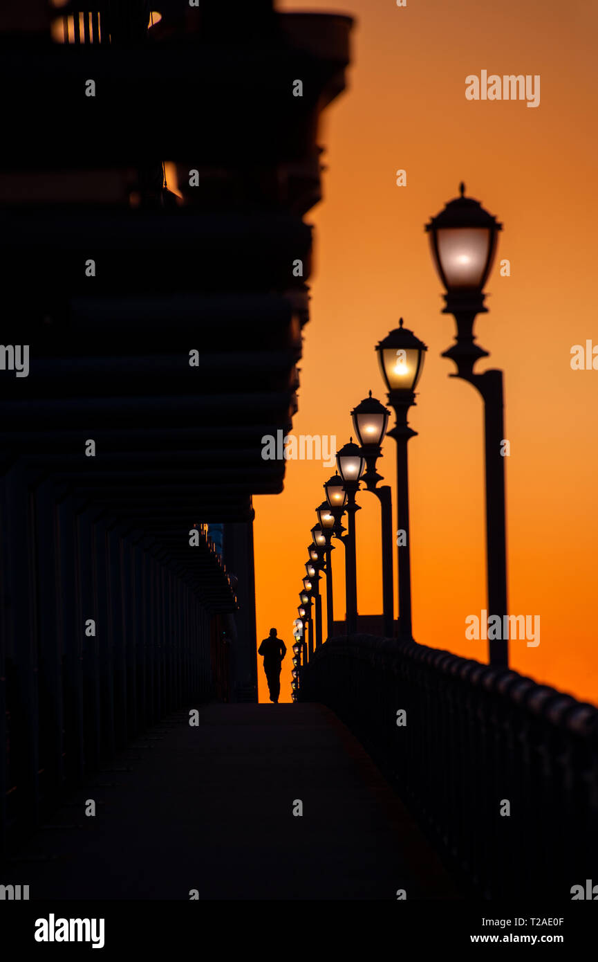Uomo che cammina oltre il ponte sulla passerella con fila di Lamposts, Philadelphia, PA, Stati Uniti d'America Foto Stock