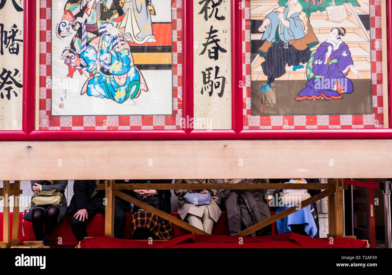 Fila di gente seduta al di fuori del teatro Kabuki-za, facce oscurate da pannelli decorativi al di fuori del teatro, Tokyo, Giappone Foto Stock