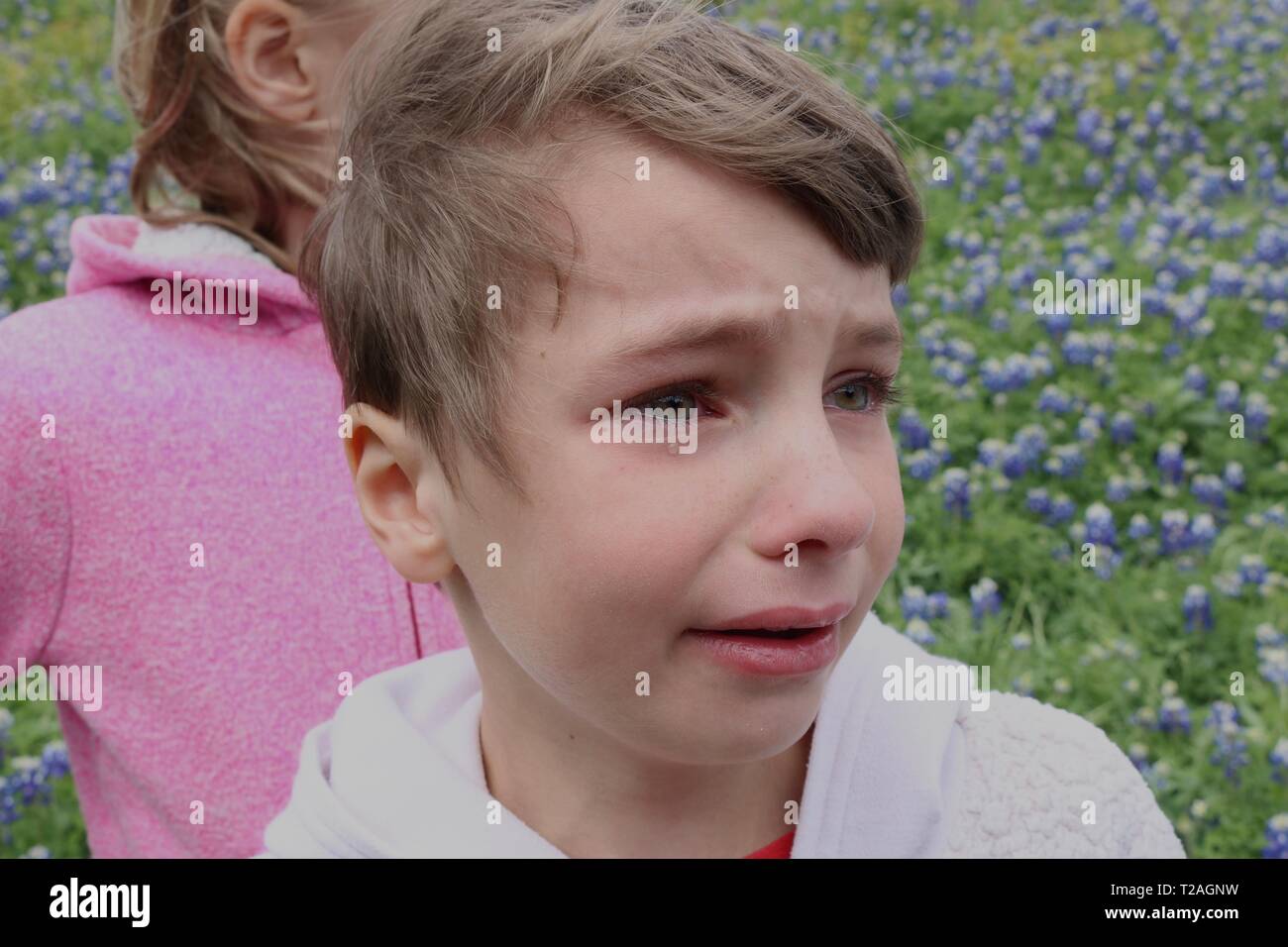 Ritratto di un bambino in un campo di fiori selvatici con uno strappo che corre lungo la sua guancia apparentemente sconvolto con sua sorella Foto Stock