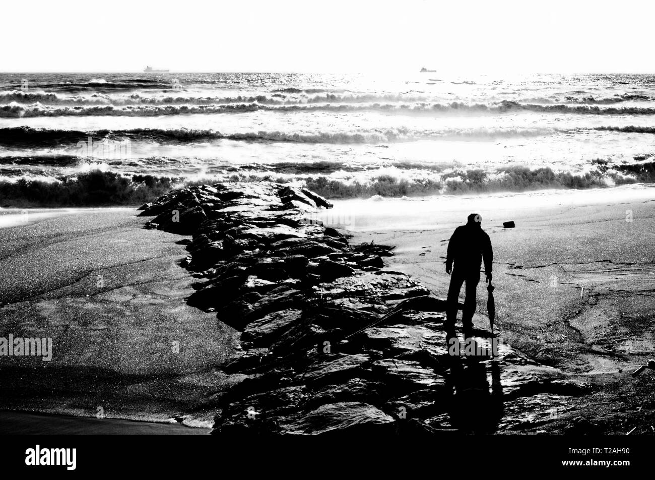 Un uomo sulla spiaggia guarda al mare mosso Foto Stock