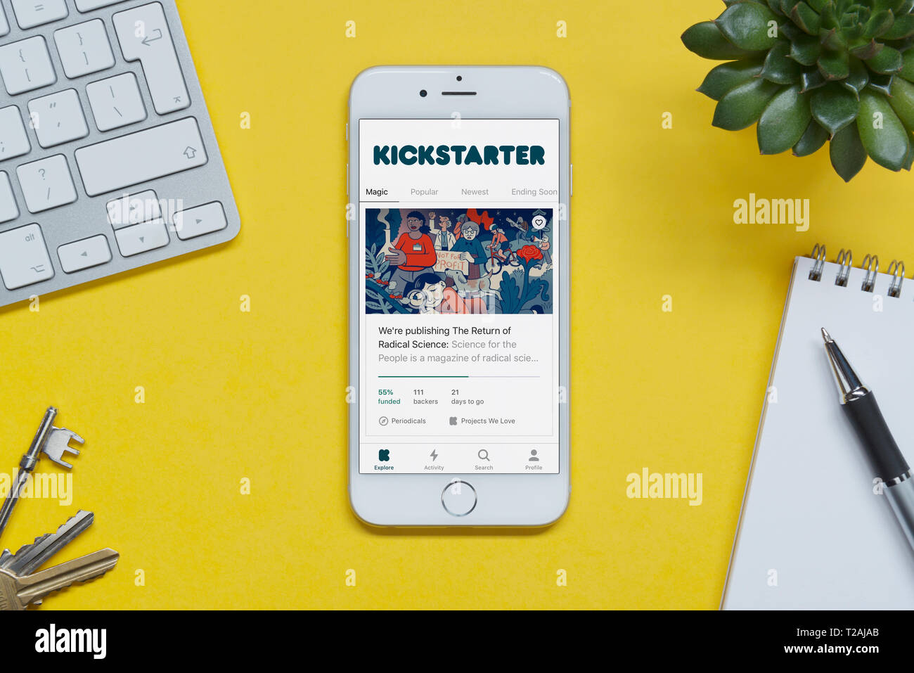 Un iPhone che mostra il sito Kickstarter poggia su uno sfondo giallo tabella con una tastiera, tasti, blocco note e di impianto (solo uso editoriale). Foto Stock