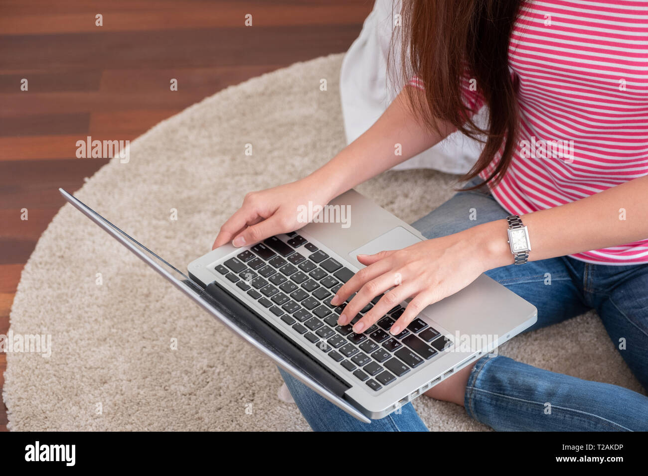 Felice donna asiatica digitando su computer portatile a casa.freelance femmina seduto su un tappeto sul pavimento il lavoro a casa in salotto Foto Stock