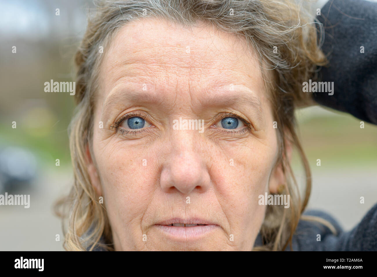 Volto di donna di mezza età con gli occhi blu, faccia rugosa e luce capelli ricci, guardando la fotocamera Foto Stock
