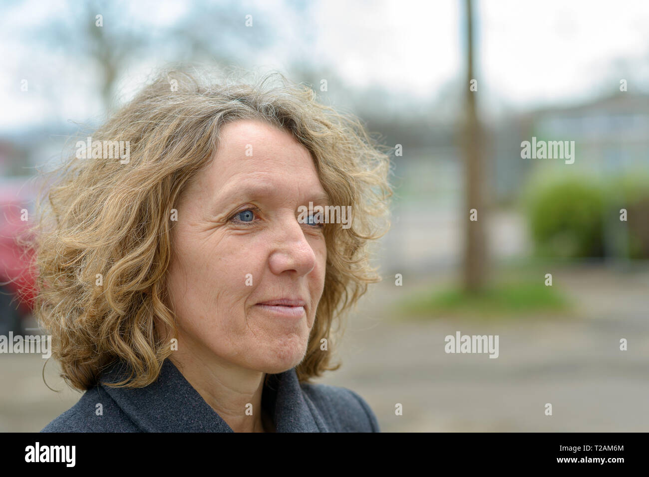 Sorridente donna attraente con tousled capelli ricci indossando un caldo cappotto invernale Foto Stock