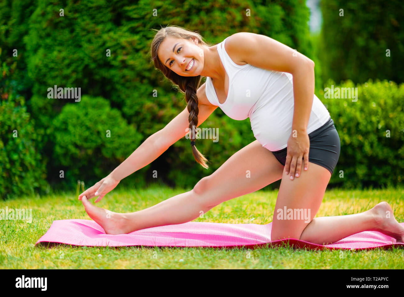 Donna incinta sorridente mentre si tocca la convergenza sul tappeto di esercizio Foto Stock